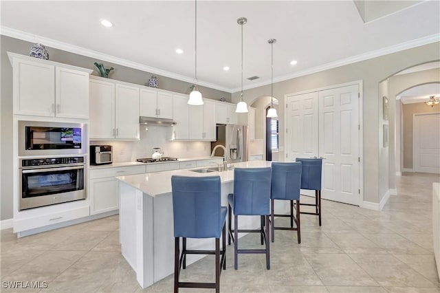 2102 Antigua Ln, Naples, FL 34120 - kitchen featuring appliances with stainless steel finishes, arched walkways, a sink, an island with sink, and white cabinetry