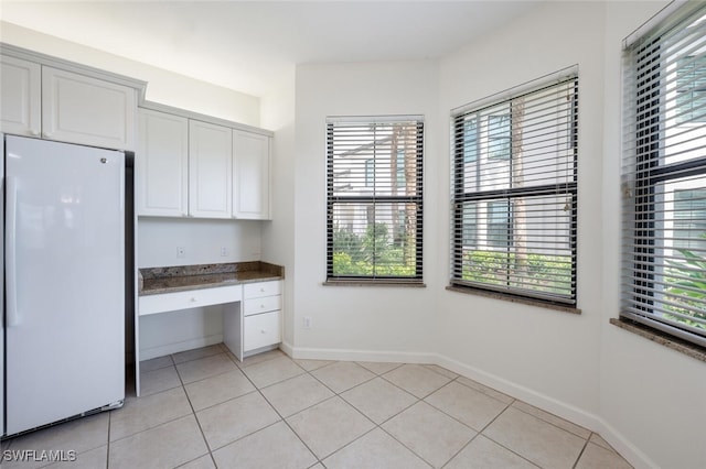 kitchen featuring freestanding refrigerator, white cabinetry, light tile patterned flooring, and baseboards