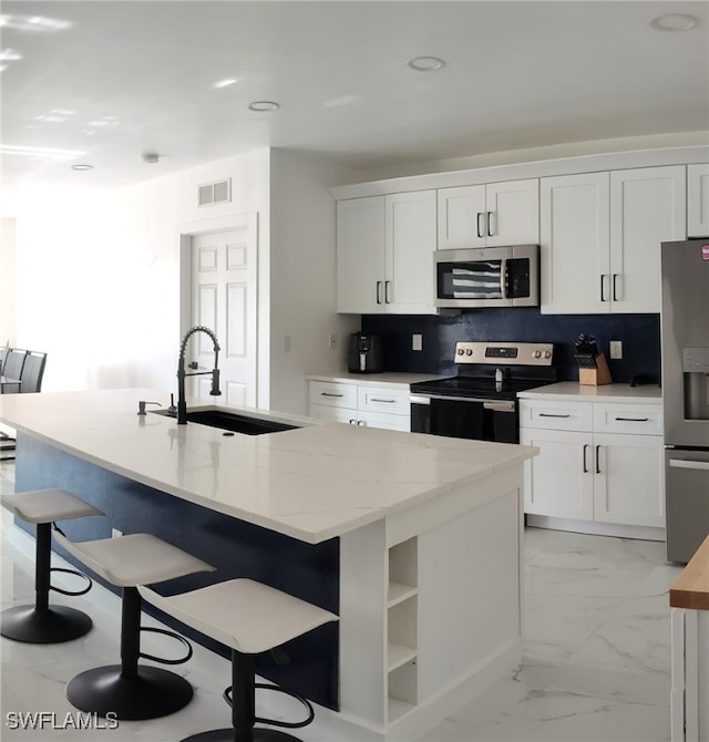 2709 SW 4th Pl, Cape Coral, FL 33914 - kitchen featuring stainless steel appliances, a sink, light marble finish flooring, white cabinetry, and a kitchen breakfast bar