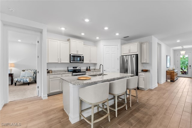 16523 Crescent Beach Way, Bonita Springs, FL 34135 - kitchen featuring stainless steel appliances, a sink, light wood finished floors, white cabinets, and an island with sink