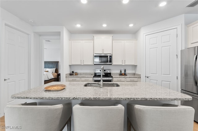 16523 Crescent Beach Way, Bonita Springs, FL 34135 - kitchen featuring appliances with stainless steel finishes, a sink, a kitchen bar, white cabinetry, and a kitchen island with sink