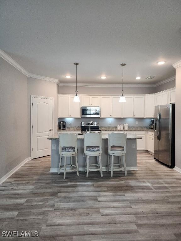 16006 Mistflower Dr, Alva, FL 33920 - kitchen with stainless steel appliances, wood finished floors, crown molding, white cabinets, and a kitchen island with sink