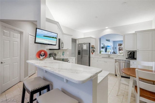 20101 Seagrove St Unit 702, Estero, FL 33928 - kitchen featuring appliances with stainless steel finishes, a sink, light tile patterned floors, a breakfast bar, and white cabinetry