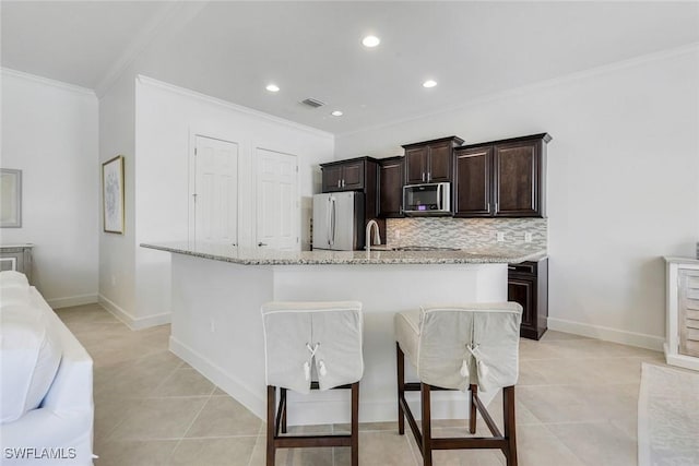 9578 Coquina Cir, Naples, FL 34120 - kitchen with stainless steel appliances, crown molding, a center island with sink, dark brown cabinets, and a kitchen bar