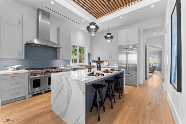 217 13th St S, Naples, FL 34102 - kitchen with wall chimney exhaust hood, high quality appliances, a kitchen island, light stone counters, and light wood-style flooring