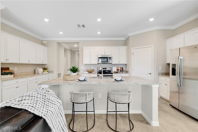 19694 Deming Ln, Estero, FL 33928 - kitchen featuring appliances with stainless steel finishes, white cabinets, a breakfast bar, a center island with sink, and crown molding
