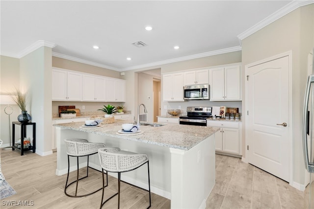 19694 Deming Ln, Estero, FL 33928 - kitchen featuring appliances with stainless steel finishes, a center island with sink, light stone countertops, white cabinets, and a breakfast bar area