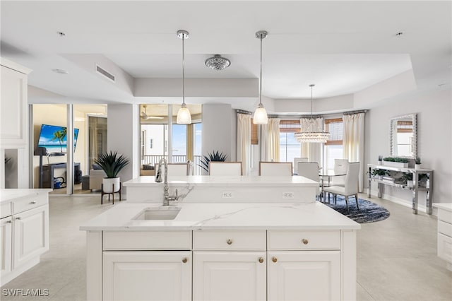 14270 Royal Harbour Ct Unit 920, Fort Myers, FL 33908 - kitchen featuring a sink, an island with sink, a raised ceiling, light stone countertops, and white cabinetry