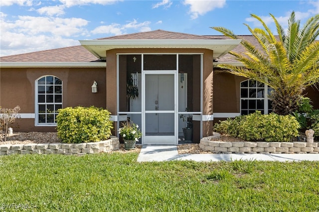 227 Manasota St, Fort Myers, FL 33913 - view of exterior entry with stucco siding, a yard, and roof with shingles