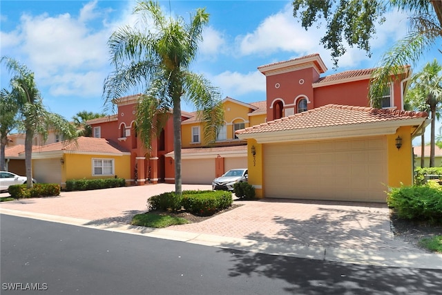 mediterranean / spanish home with a tile roof, stucco siding, decorative driveway, a residential view, and an attached garage