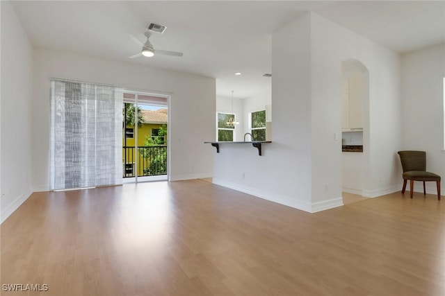 unfurnished living room featuring light wood-style floors, arched walkways, a ceiling fan, baseboards, and recessed lighting