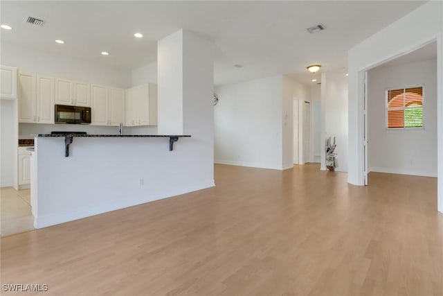kitchen featuring black microwave, a kitchen bar, light wood-style flooring, and recessed lighting
