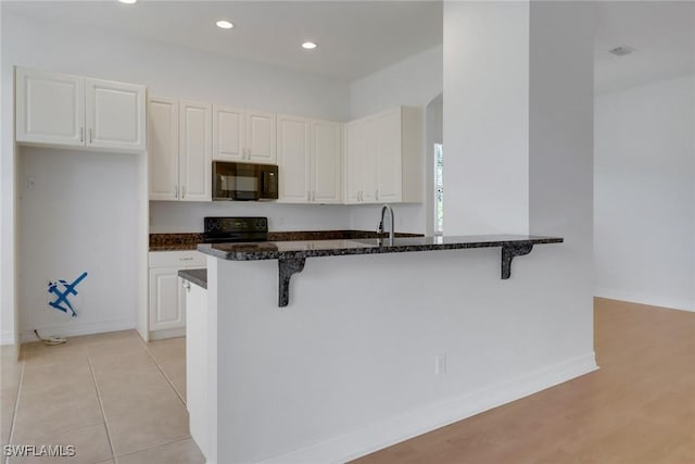kitchen with black appliances, a kitchen breakfast bar, dark stone counters, white cabinets, and recessed lighting