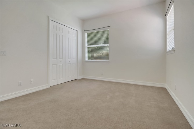 unfurnished bedroom featuring light colored carpet, multiple windows, baseboards, and a closet