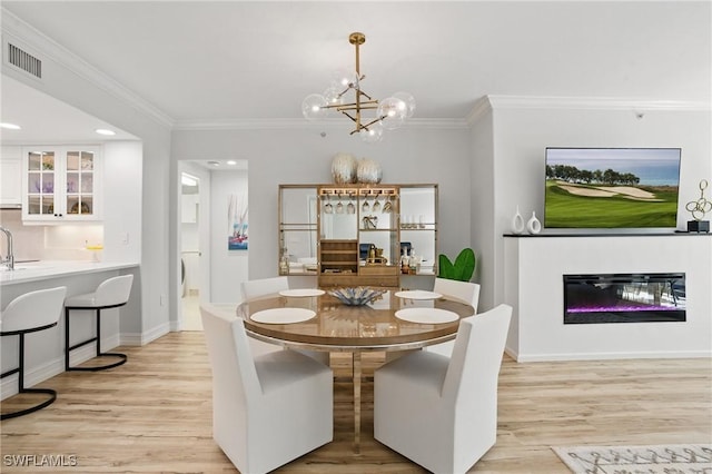 2728 Tiburon Blvd E Unit A104, Naples, FL 34109 - dining area with light wood-style flooring, a glass covered fireplace, crown molding, a chandelier, and baseboards