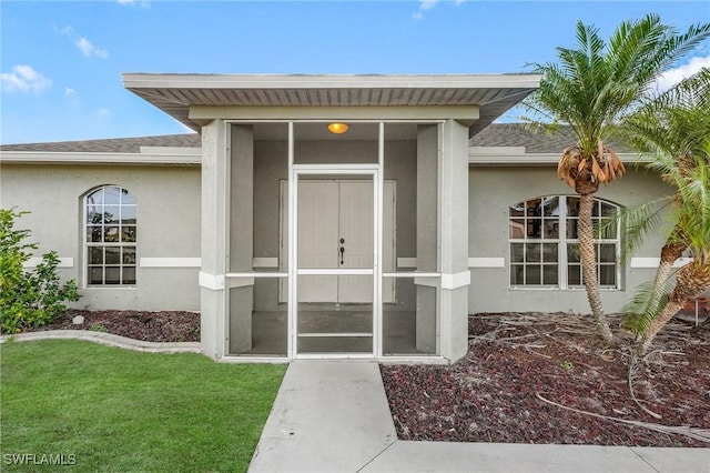 1233 NW 26th Pl, Cape Coral, FL 33993 - view of exterior entry featuring stucco siding, a shingled roof, and a yard