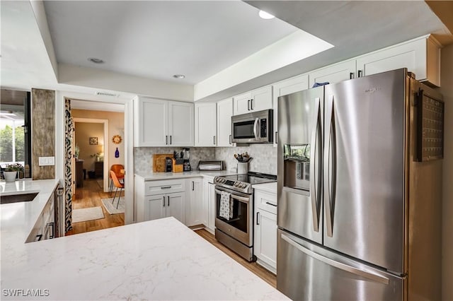 5692 Eichen Cir W, Fort Myers, FL 33919 - kitchen featuring appliances with stainless steel finishes, wood finished floors, white cabinetry, tasteful backsplash, and light stone counters
