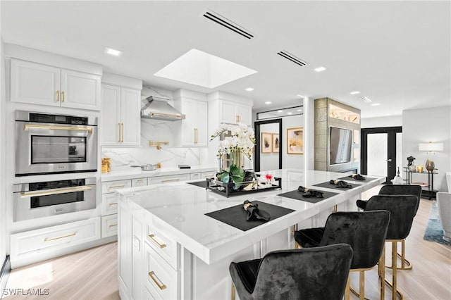 6212 Cocos Dr, Fort Myers, FL 33908 - kitchen with double oven, wall chimney exhaust hood, a kitchen island, light wood-style floors, and light stone countertops