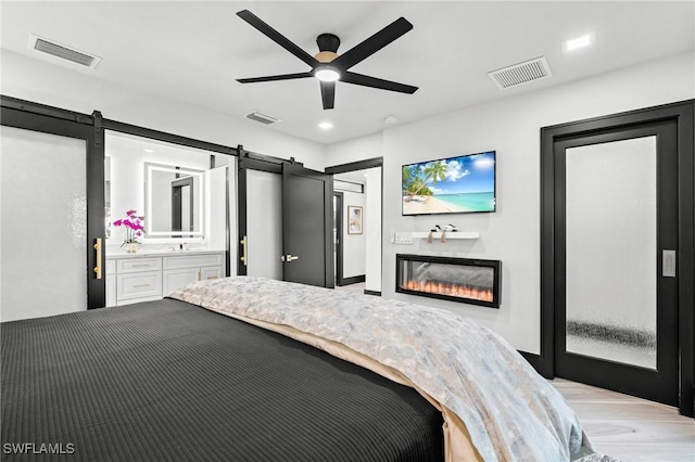 6212 Cocos Dr, Fort Myers, FL 33908 - bedroom featuring a barn door, ceiling fan, a glass covered fireplace, and light wood finished floors