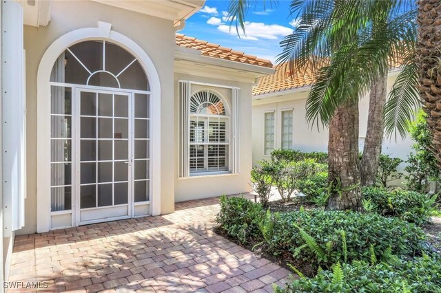 3774 Whidbey Way, Naples, FL 34119 - doorway to property featuring stucco siding, a patio, and a tiled roof