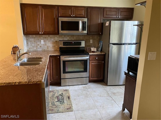 kitchen featuring appliances with stainless steel finishes, a sink, light stone countertops, a peninsula, and tasteful backsplash
