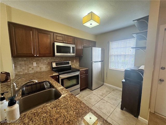kitchen featuring appliances with stainless steel finishes, a sink, decorative backsplash, dark stone countertops, and baseboards