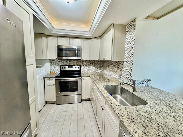 3625 Boca Ciega Dr Unit 110, Naples, FL 34112 - kitchen featuring stainless steel appliances, a sink, washer / clothes dryer, a raised ceiling, and ornamental molding