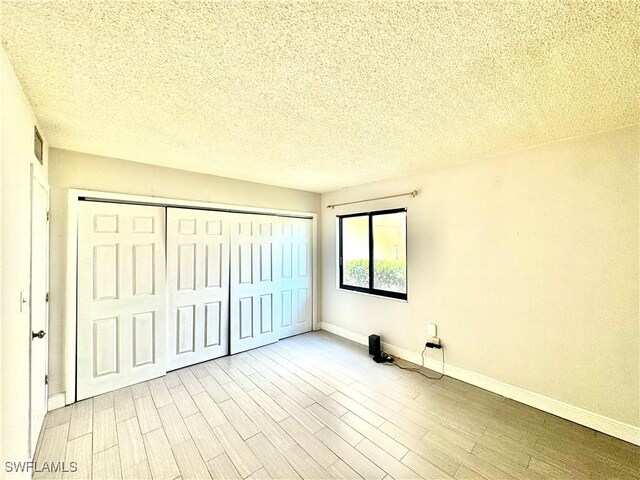 3625 Boca Ciega Dr Unit 110, Naples, FL 34112 - unfurnished bedroom with a textured ceiling, a closet, baseboards, and wood finished floors