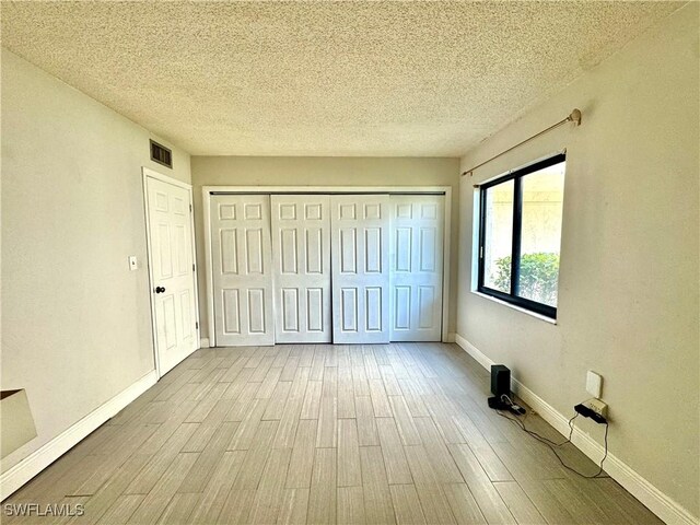 3625 Boca Ciega Dr Unit 110, Naples, FL 34112 - unfurnished bedroom with wood finished floors, a textured ceiling, baseboards, and a closet