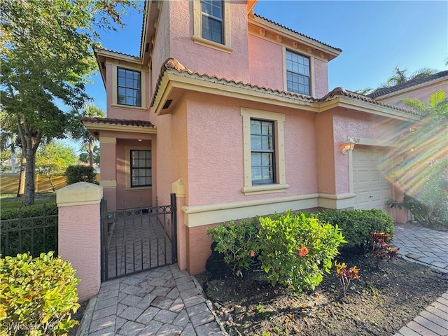 view of front of home with stucco siding, a garage, fence, and a gate