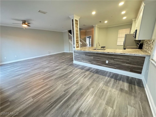 kitchen featuring ornamental molding, baseboards, wood finished floors, light stone counters, and refrigerator