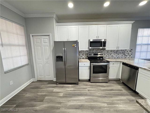 kitchen with appliances with stainless steel finishes, crown molding, white cabinets, backsplash, and light stone counters