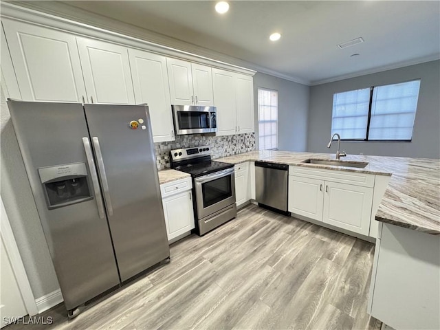 kitchen with stainless steel appliances, a sink, ornamental molding, white cabinetry, and light wood-style floors