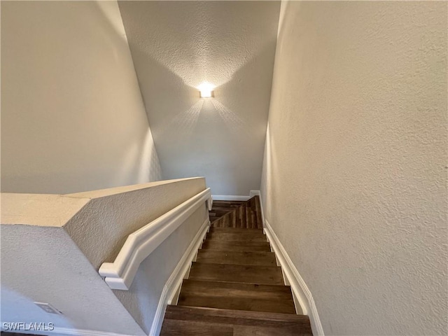 stairway with wood finished floors, a textured wall, and baseboards
