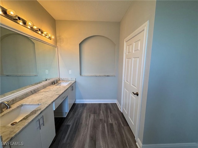 bathroom with wood finished floors, baseboards, double vanity, and a textured ceiling