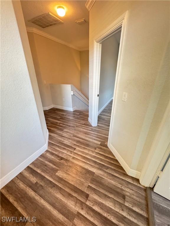 hallway featuring wood finished floors, baseboards, crown molding, and an upstairs landing