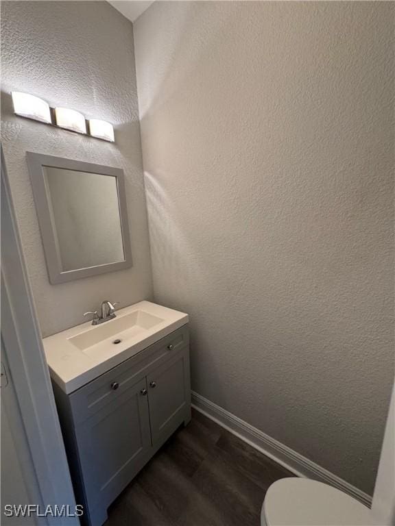 bathroom featuring wood finished floors, vanity, toilet, baseboards, and a textured wall