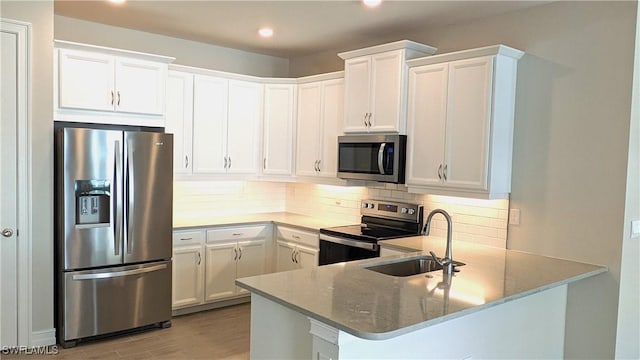 986 Enbrook Loop, Naples, FL 34114 - kitchen featuring stainless steel appliances, a sink, backsplash, a peninsula, and light wood-style flooring