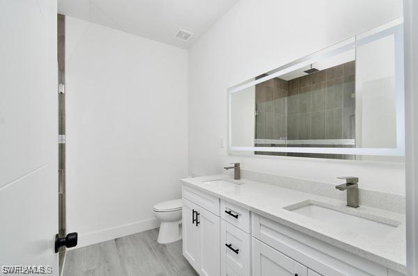 8304 Lena Ct, Labelle, FL 33935 - bathroom featuring toilet, wood finished floors, baseboards, double vanity, and a tile shower