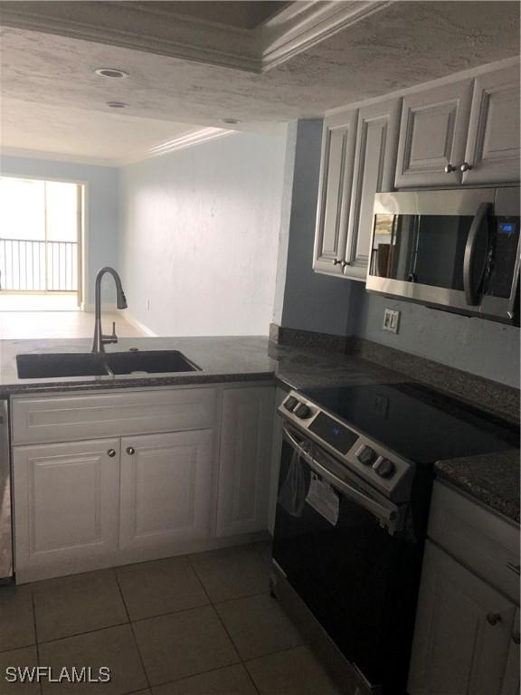 4510 N Key Dr Unit 302, North Fort Myers, FL 33903 - kitchen with appliances with stainless steel finishes, a sink, light tile patterned flooring, white cabinetry, and ornamental molding