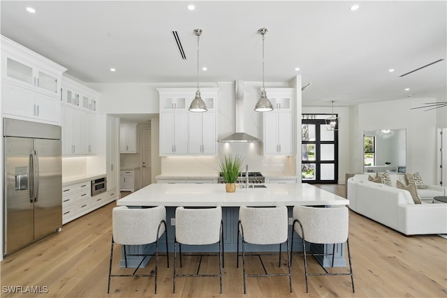 24721 Bay Bean Ct, Bonita Springs, FL 34134 - kitchen featuring stainless steel built in refrigerator, wall chimney range hood, open floor plan, a kitchen island with sink, and white cabinetry