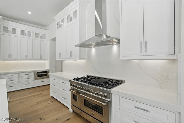 24721 Bay Bean Ct, Bonita Springs, FL 34134 - kitchen featuring appliances with stainless steel finishes, wall chimney exhaust hood, white cabinets, light stone counters, and light wood-style flooring