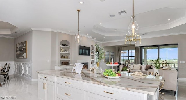 15315 Lucerna St Unit 201, Naples, FL 34114 - kitchen featuring a raised ceiling, open floor plan, crown molding, light stone counters, and a lit fireplace