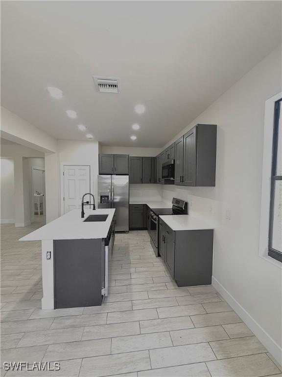 2917 50th St W, Lehigh Acres, FL 33971 - kitchen featuring stainless steel appliances, a sink, light countertops, baseboards, and a kitchen island with sink