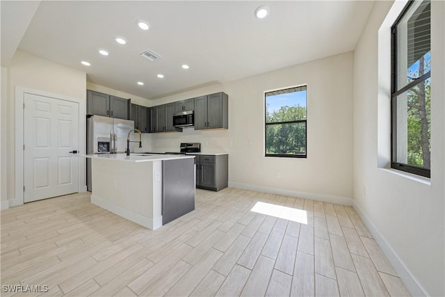 2907 55th St W, Lehigh Acres, FL 33971 - kitchen featuring appliances with stainless steel finishes, light countertops, recessed lighting, light wood finished floors, and a kitchen island with sink