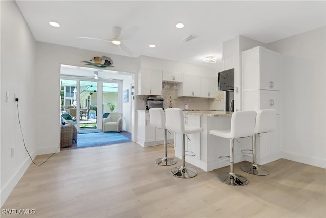 3905 Del Prado Blvd S Unit D-101, Cape Coral, FL 33904 - kitchen with ceiling fan, white cabinetry, a kitchen breakfast bar, a peninsula, and light wood finished floors