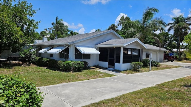27625 Michigan St, Bonita Springs, FL 34135 - view of front facade with a sunroom, a front yard, concrete driveway, a garage, and a shingled roof
