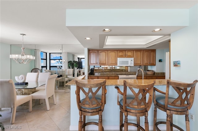 300 S Collier Blvd Unit 2304, Marco Island, FL 34145 - kitchen featuring white microwave, a kitchen bar, light tile patterned floors, light stone countertops, and brown cabinetry