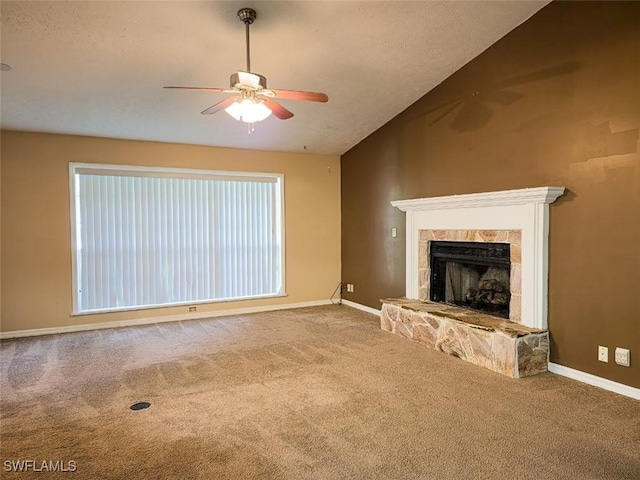 unfurnished living room with carpet, ceiling fan, lofted ceiling, a stone fireplace, and baseboards