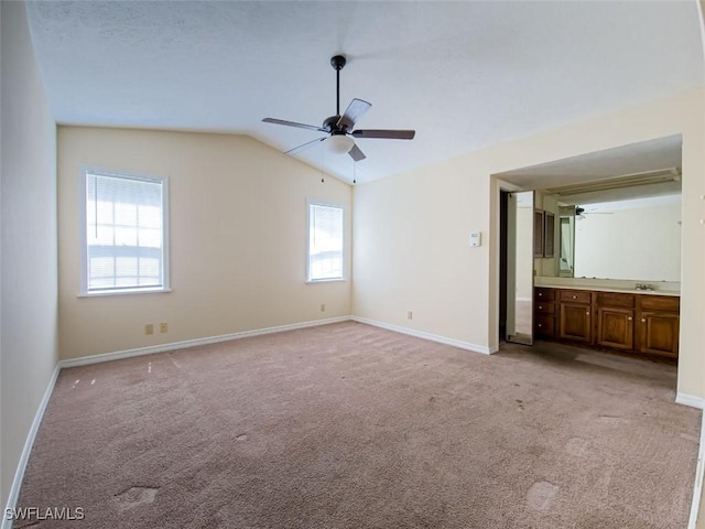 unfurnished bedroom with light carpet, vaulted ceiling, baseboards, connected bathroom, and a ceiling fan